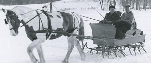 一匹马拉着雪橇穿过雪地的黑白照片. 一个男人和一个女人坐在雪橇上.